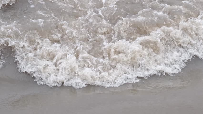 River swollen with meltwater, rushing through valley, its banks eroded and muddy.