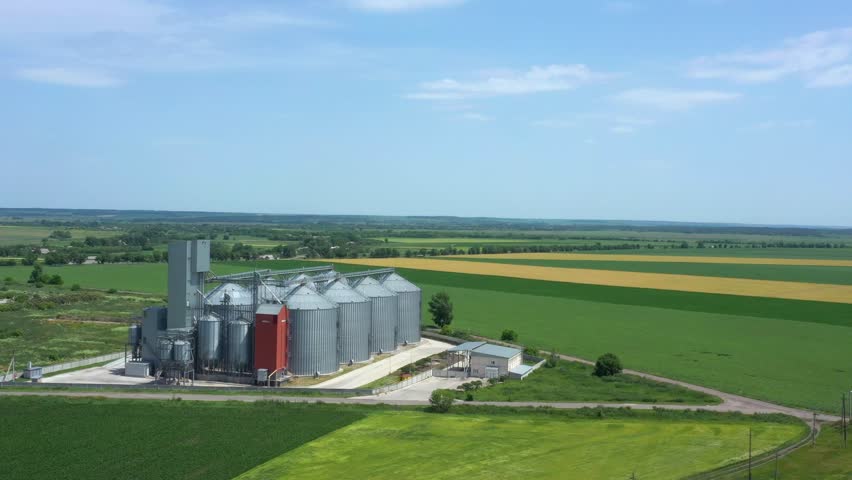 modern grain silos elevator at the field of blooming sunflowers aerial view
