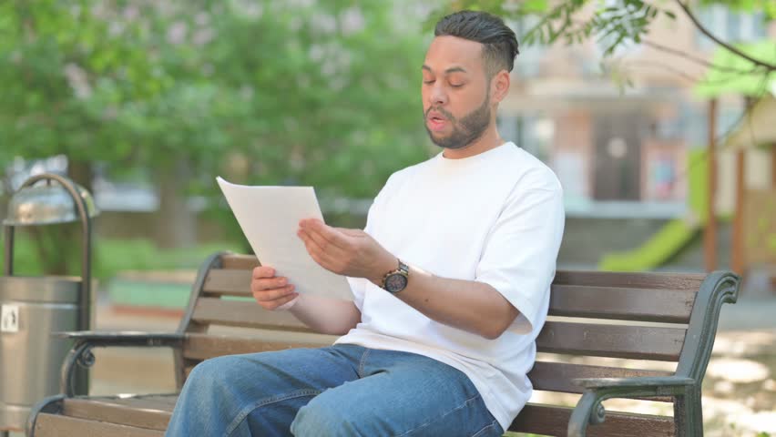 Young Man Celebrating Documents while Sitting Outdoor on Bench