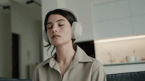 Young woman in a beige shirt, eyes closed, wearing headphones while relaxing at home. Concept of relaxation, music, and serenity. Young Woman Listening to Music with Headphones in Modern Home - Powered by Shutterstock - Get 15% off with code: PIKWIZARD15