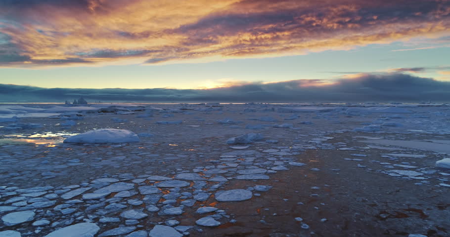 Arctic frozen ocean winter sunset landscape aerial view. Ice floes and snow covered icebergs under bright colorful evening sky. Antarctica travel and exploration. Discover the beauty of South Pole