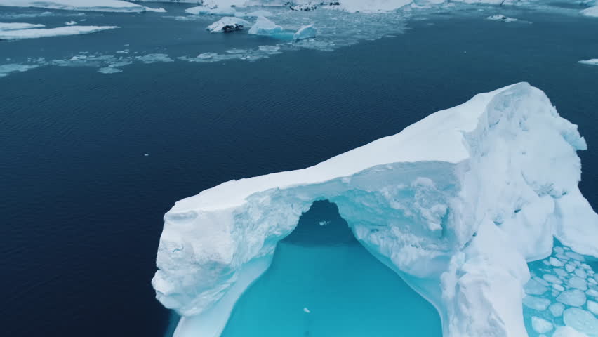 Blue melting ice cave iceberg floating dramatic ocean landscape. Huge towering frozen arch glacier melting underwater. Climate change at polar winter scene. Travel to Antarctica. Aerial drone footage