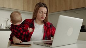 Young Woman with adorable baby boy on her knees sitting by table in front of laptop in the kithen, typing and looking through data on screen - Powered by Shutterstock - Get 15% off with code: PIKWIZARD15
