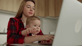 Woman sitting at home working and holding her baby boy on a lap. Typing on keyboard. Maternity trouble - Powered by Shutterstock - Get 15% off with code: PIKWIZARD15