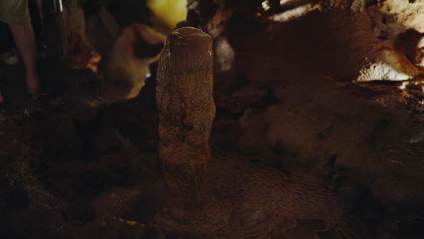 Low-light image of a stalagmite rising from the cave floor with intricate details and textures, captured in a Portuguese cave. Mysterious Stalagmite Formation Inside a Dark Cave