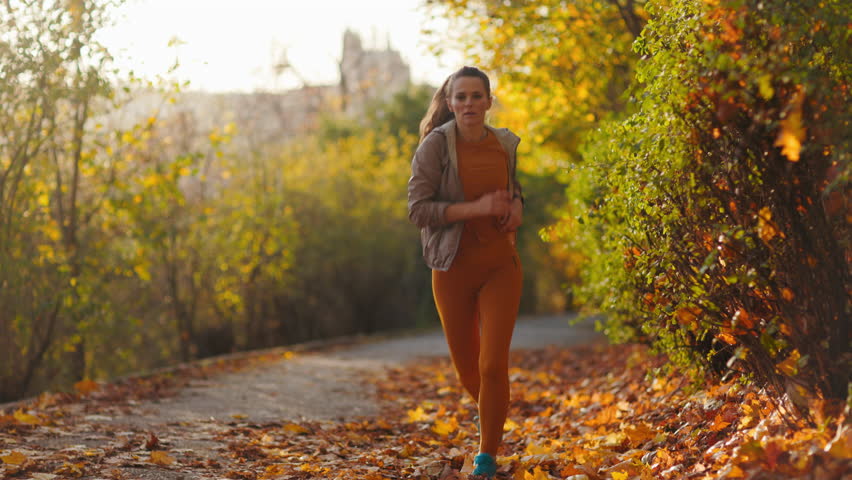 Hello autumn. stylish middle aged woman in fitness clothes in the park running.