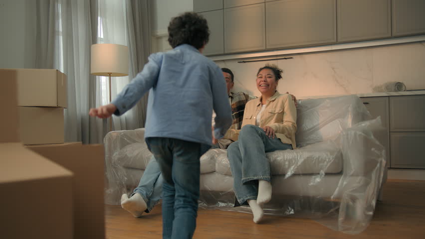 African american family funny carefree little boy kid child playing running to parents happy home owners mom dad son hugging sit on sofa together celebrate moving day relocation new apartment mortgage