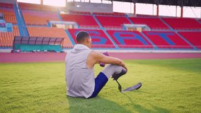 Asian para-athlete with prosthetic blades stretching leg in stadium. Attractive amputee sportsman runner sitting on floor, taking a break after practicing workout for Paralympics running competition. - Powered by Shutterstock - Get 15% off with code: PIKWIZARD15