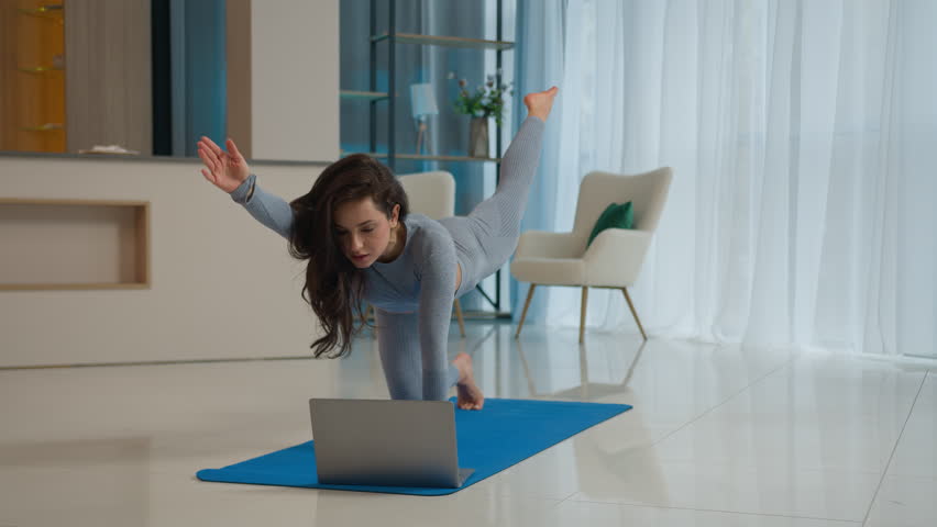 Yoga class with laptop workout video tutorial online training at home fit Caucasian woman sport trainer girl yogi female sportswoman doing exercise raise leg hand learning asana fitness pilates on mat