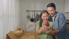 Asian mature man surprise and give rose flower to his beautiful wife. Attractive romantic couple male and woman spending time to celebrate anniversary and valentine's day together in kitchen at home. - Powered by Shutterstock - Get 15% off with code: PIKWIZARD15