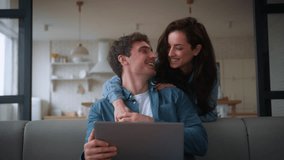 Caucasian couple family at home man guy freelancer male husband boyfriend using laptop on couch sofa girl female woman girlfriend wife going from kitchen hugging back talking discuss computer shopping - Powered by Shutterstock - Get 15% off with code: PIKWIZARD15