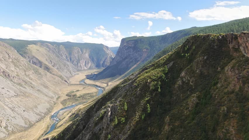 Flying over a narrow valley overgrown with forest between the mountains. A fast mountain river with amazing green water. River valleys.