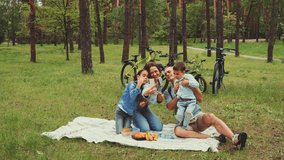 Happy family enjoys picnic in forest park, taking selfie together with bicycles in background. Parents and two children sit on blanket surrounded by trees and their bicycles, joyful moment in nature - Powered by Shutterstock - Get 15% off with code: PIKWIZARD15