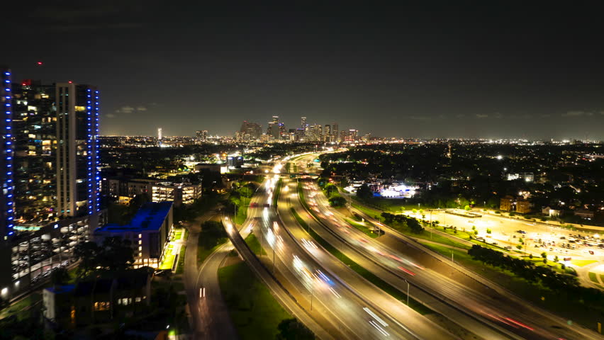 Hyperlapse of bustling night traffic on a houston highway, with dazzling light trails and the city skyline aglow in the distance of this major American city