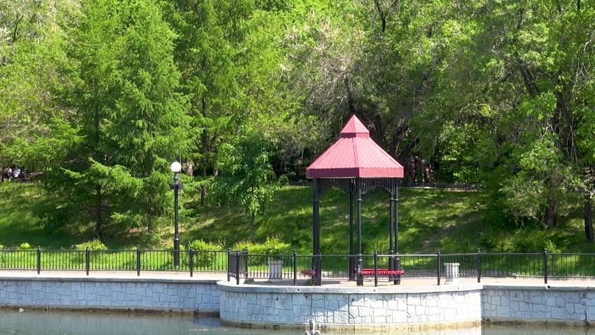 General view of the park with a sidewalk, lawn, trees and gazebos