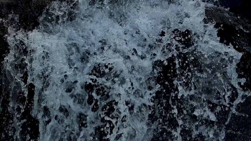 Close-up shot of the waterfall flowing over the rocks, creating white foam
