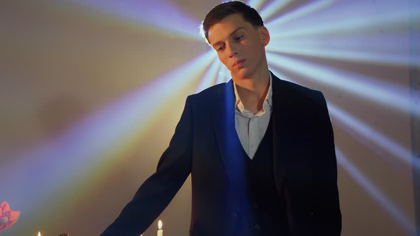 Portrait of a young man in a jacket in a nightclub in the rays of a spotlight. The guy holds a bottle of alcohol in his hands and looks at the woman. Flirting, nightlife, passion.