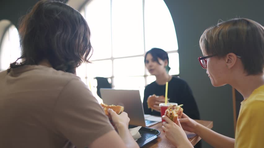 group of students sit in a cafe and do a lifestyle project on a laptop together. business concept of modern training and development. students discuss their homework and eat fast food burgers
