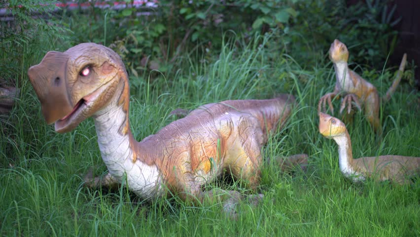 Against the background of the grass, the oviraptor blinks its eyes. The effect of eye movement. A dinosaur is a small bird with a beak. High quality 4k footage