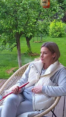Woman smokes hookah on in backyard. Outdoor recreation with friends Vertical video. Taken from hand. High quality 4k footage