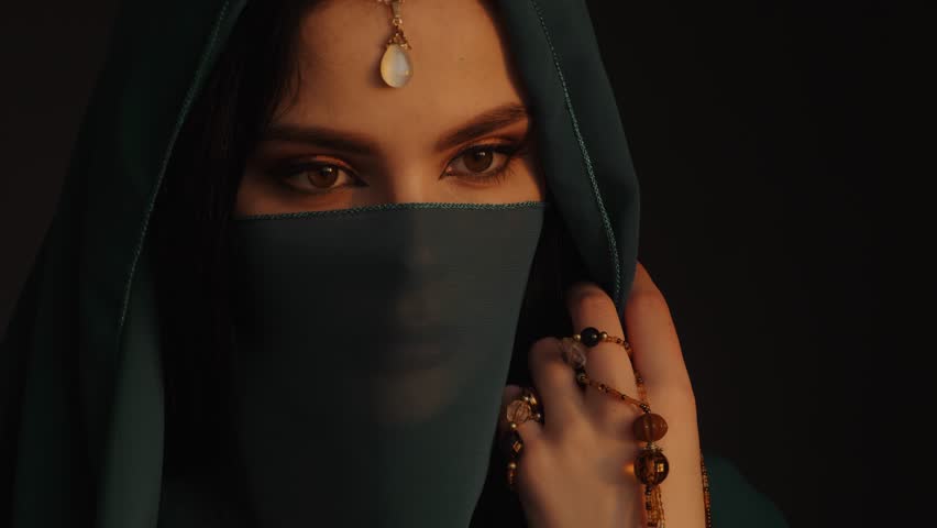 Beautiful sensual woman in traditional costume. Romantic portrait of young girl with perfect bright makeup wearing traditional jewelry standing indoors against dark background. Fine art 4K UHD footage