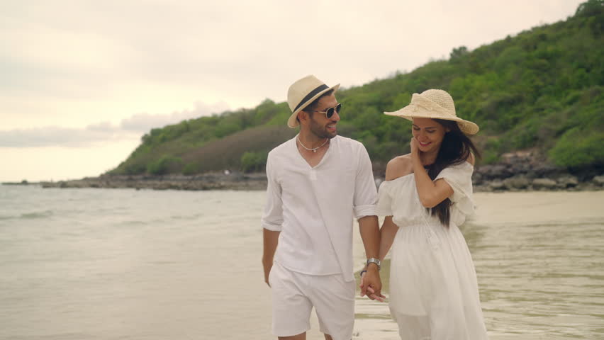 4K Happy Caucasian couple enjoy and fun outdoor lifestyle travel nature at the sea on summer beach holiday vacation. Man and woman walking and playing together at tropical island beach at sunset. 