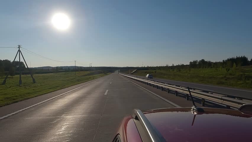 View back to the road on a summer day from a red car. Highways and roadsides move away from the car.