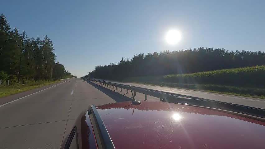 View back to the road on a summer day from a red car. Highways and roadsides move away from the car.