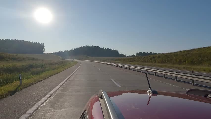 View back to the road on a summer day from a red car. Highways and roadsides move away from the car.