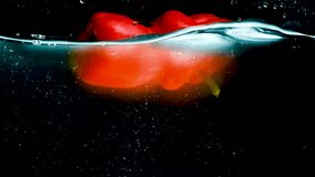 Red bell peppers on a black background submerge in water, rotate, float to the surface and form bubbles. Slow motion mode. Close-up. - Powered by Shutterstock - Get 15% off with code: PIKWIZARD15