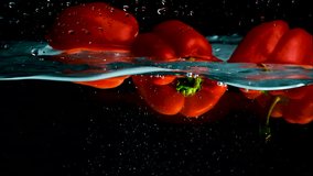 Red bell peppers on a black background submerge in water, rotate, float to the surface and form bubbles. Slow motion mode. Close-up. - Powered by Shutterstock - Get 15% off with code: PIKWIZARD15