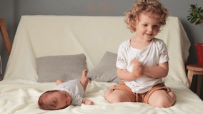 Childcare and sibling love. Smiling blond wavy haired older sister playing with her newborn baby brother sitting on white sofa in living room loving sister with baby - Powered by Shutterstock - Get 15% off with code: PIKWIZARD15