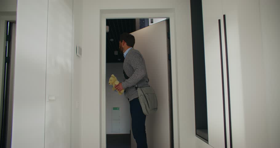 Charming Caucasian man coming back home from business trip. Greeting with his little daughter. Presenting gift for little child. Giving teddy bear to beloved girl. Wife hugging her husband.