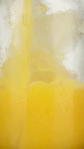 Pouring Fresh Orange Juice into Glass with Ice, extreme macro. sstkVertical