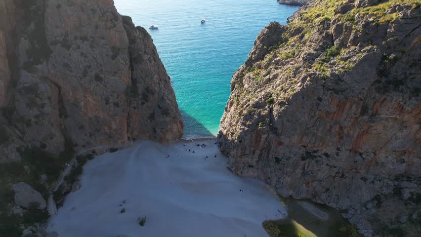 4K Aerial Drone video of unique beach carved into the canyon with turquoise blue water and boats anchored, Sa Calobra Beach, Mallorca, Spain