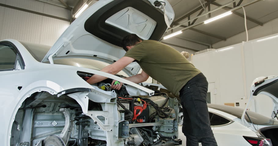A mechanic works diligently on a vehicle in a clean, well-organized auto repair shop, focusing on car body repair and electrical systems. Mechanic Repairing Car in Modern Auto Workshop