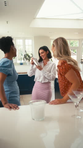 Vertical video of three mature female friends at home having fun mixing and drinking cocktails together - shot in slow motion