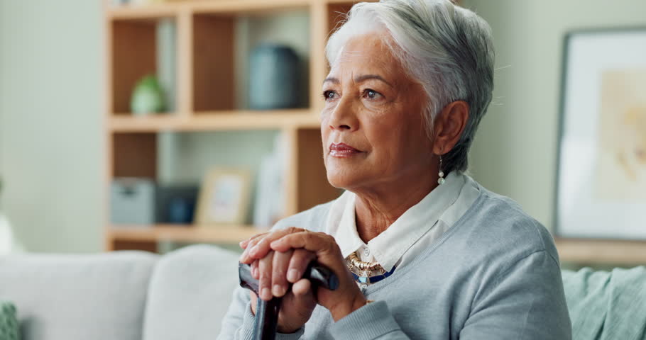 Sofa, thinking and person with disability with cane for arthritis, healthcare or support in living room. Elderly woman, walking stick and sad on couch for retirement, assistance or help at home