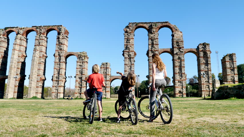 Happy family with bike enjoying view of ancient roman Miracali Aqueduct in Merida- Spain