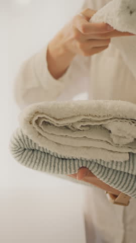Vertical position. A young housewife carefully puts laundry and clothes in piles, showing concern for cleanliness order. She puts things in order in her home wardrobe, things lay neatly on the shelves