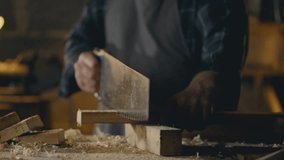 A woodworking carpenter saws off a board with a hand saw. The process of processing wooden boards in a workshop for making solid wood furniture. An experienced carpenter is in an authentic workshop - Powered by Shutterstock - Get 15% off with code: PIKWIZARD15