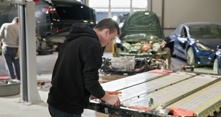 Male technician repairing a high-capacity lithium-ion battery module for an electric vehicle in a modern automotive repair shop. Technician Working On EV Battery In Car Repair Shop