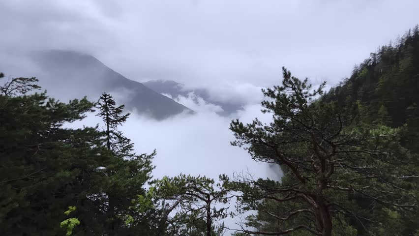 4K footage of high altitude mountain view in valley full of mist on European Alps, the mist is enshrouding the hills and trees in thick white fog, This footage was taken on Alps, in Italy in Spring
