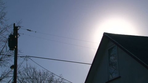 Time lapse during sunrise on blue sky day with star burst revealing itself from behind house.