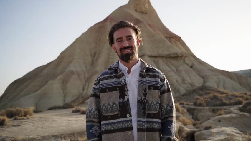 Smiley portrait of handsome caucasian man looking at camera standing next to a sandcastle at desert in Spain. 