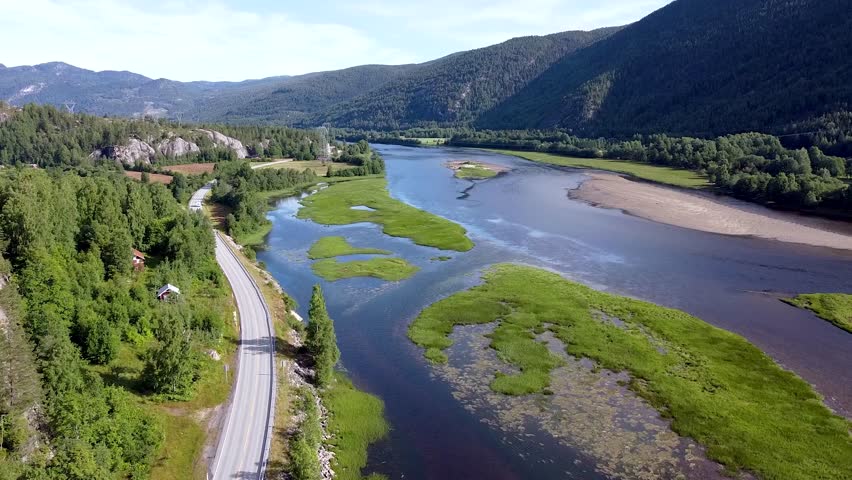 Drone footage showcasing a picturesque Norwegian landscape with lush greenery, a winding river, and surrounding mountains under clear skies.
