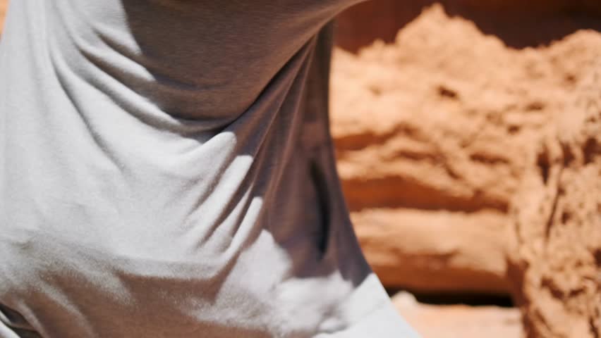 Walking in nature among sandy rocks dancing fashionable hipster in raincoat and hat enjoying vacation in summer. Slow motion.
