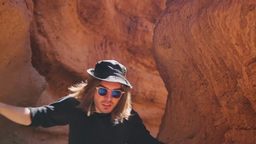 Fashion guy dances, wriggling like a snake, standing among the mountain rocks of red sandstone, hipster staged a dance performance in nature.