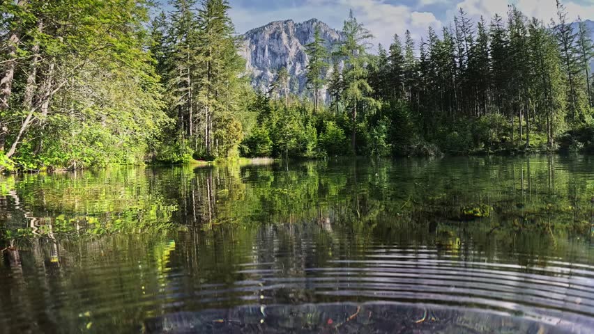 Half underwater dome shot of Green Lake - Gruner See - in Austria. Camera plunges into the water of lake with green bottom, Alps mountains in the background