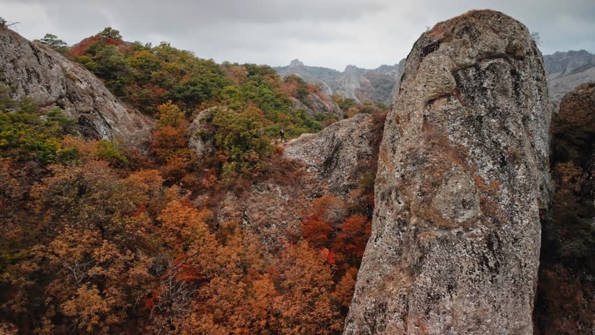 Stunning aerial drone footage of man standing on the rocky cliffs of the Birtvisi Mountains in Georgia during autumn season. He enjoys an active weekend vacation exploring the majestic landscape